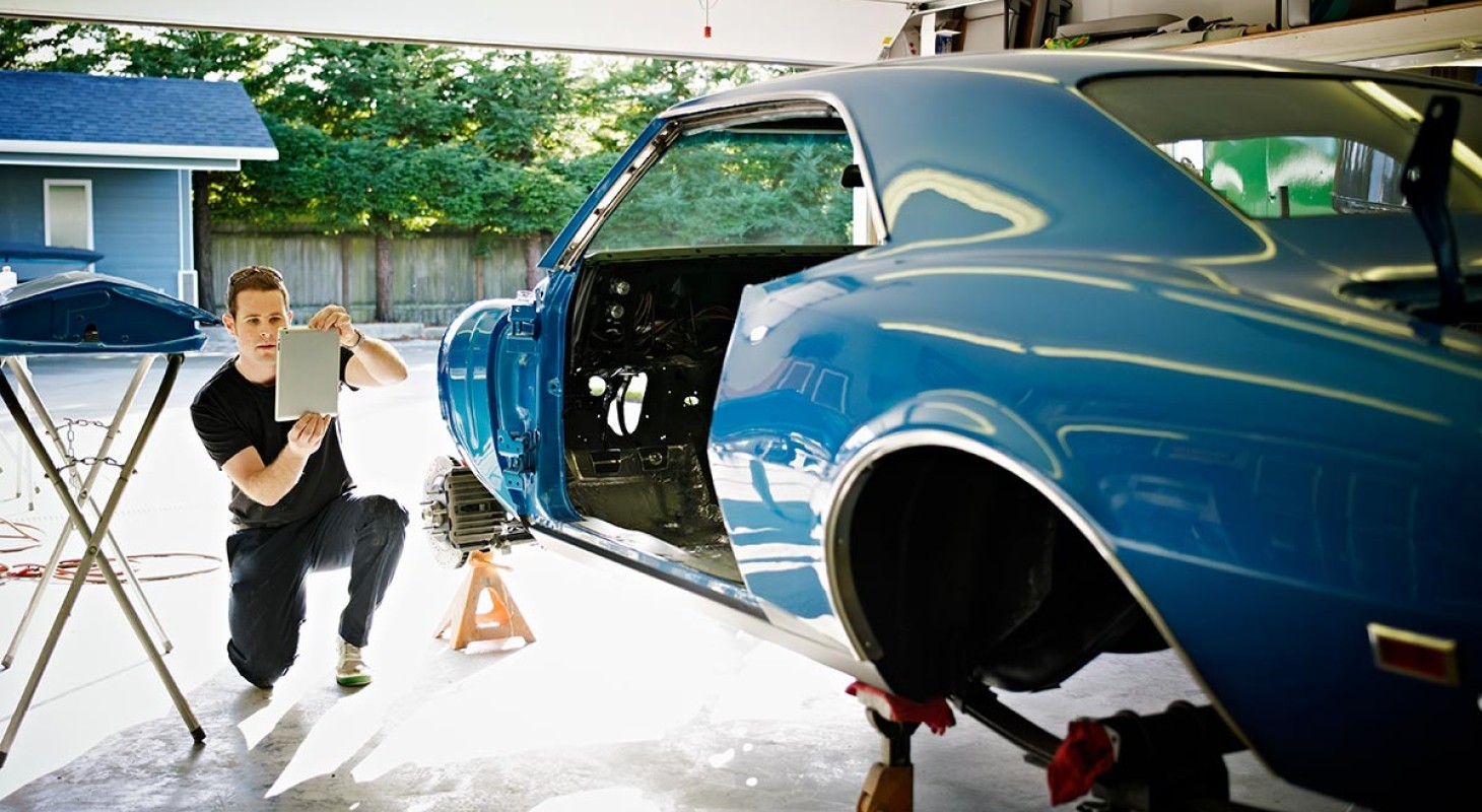 man working on blue classic car in a garage