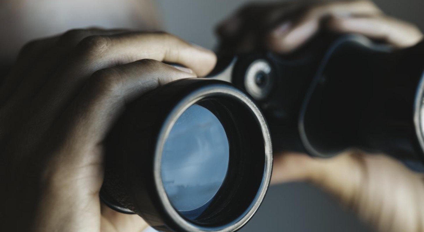 close-up of hands holding binoculars with blue sky reflecting in lens