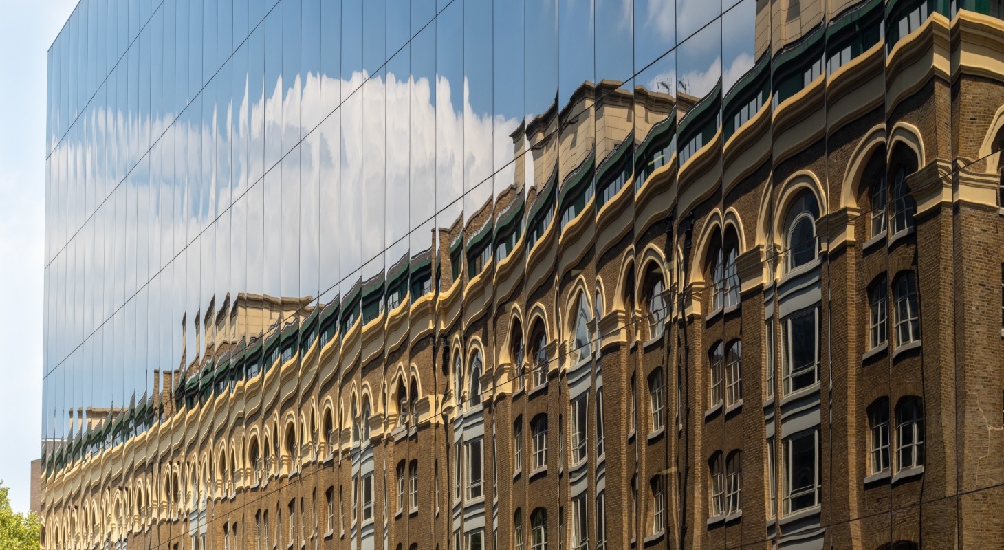 old office building reflected in the facade of new glass building