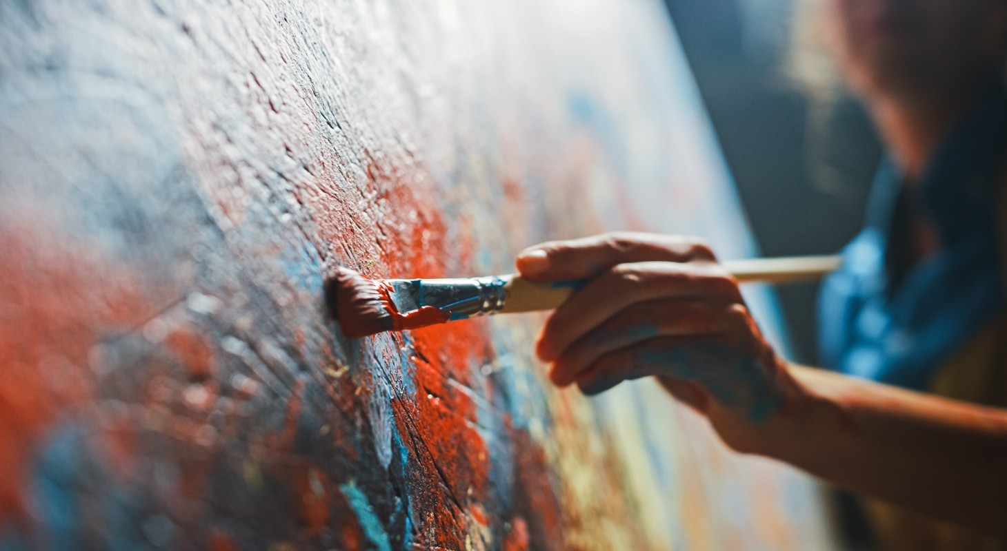 older female artist paints on closeup of red and blue canvas