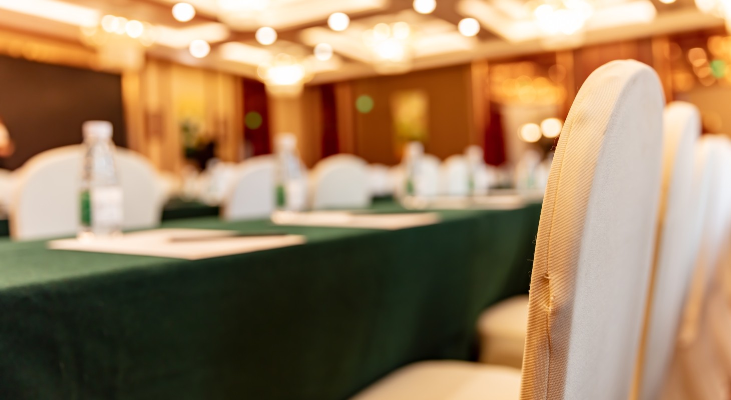 blurred view of large empty conference room with gold chairs and green tablecloths