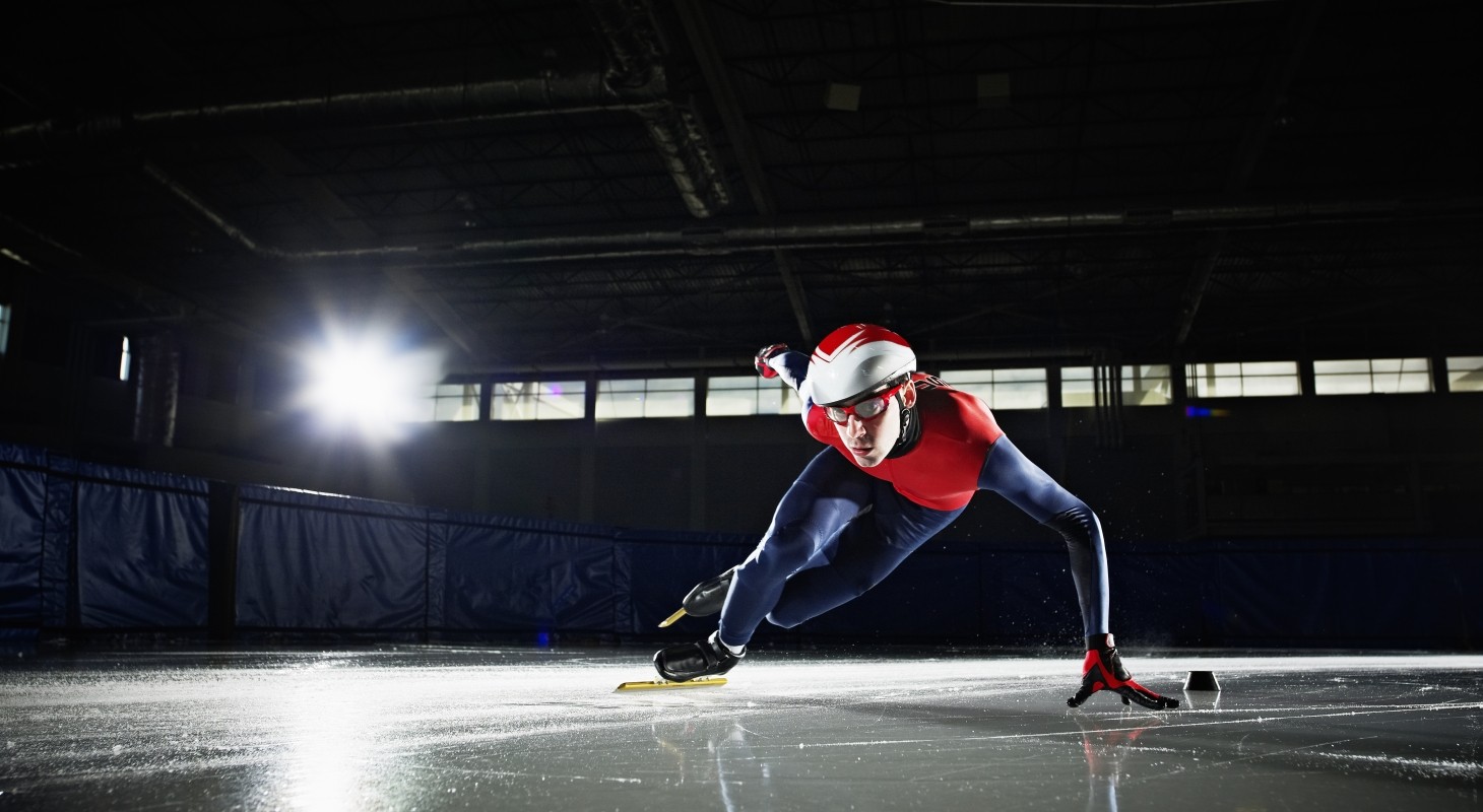 short track speed skater in dark rink with red and blue uniform
