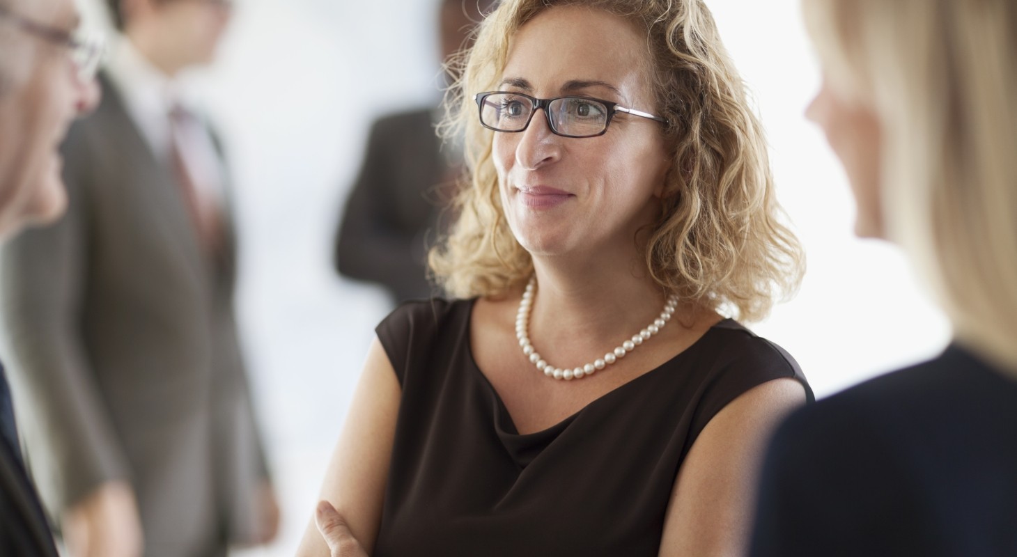 female executive with arms crossed smiling and talking to colleagues