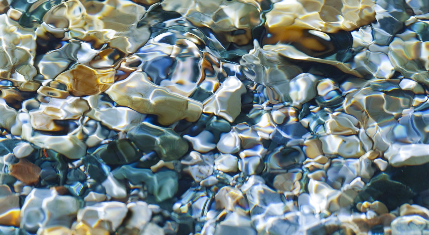 sunlight shining through water to illuminate multi-colored pebbles below