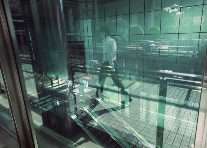 reflection of man walking in front of green glass office building