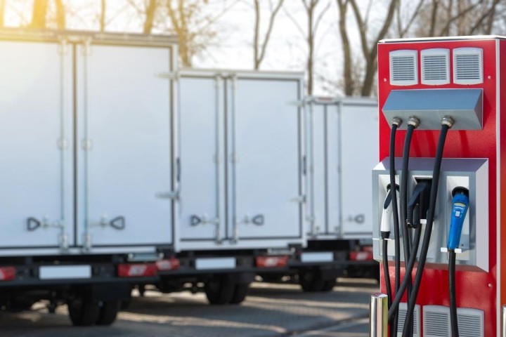 row of electric box delivery trucks behind red charging station