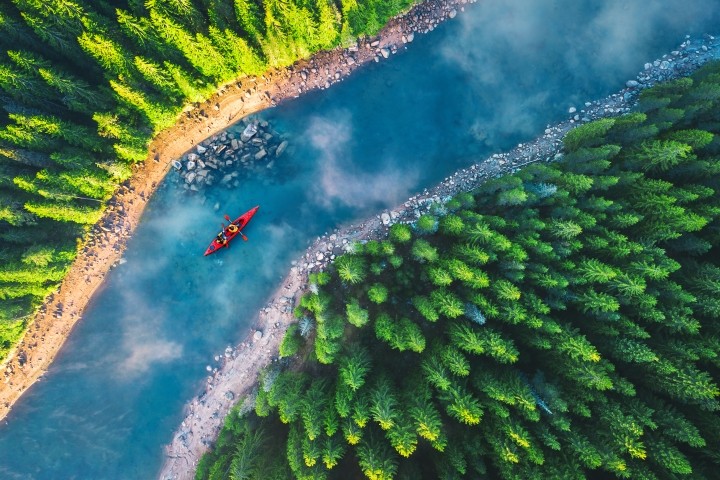 aerial view of red kayak on blue river between green forests