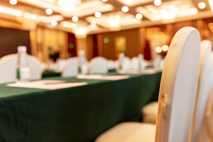 blurred view of large empty conference room with gold chairs and green tablecloths