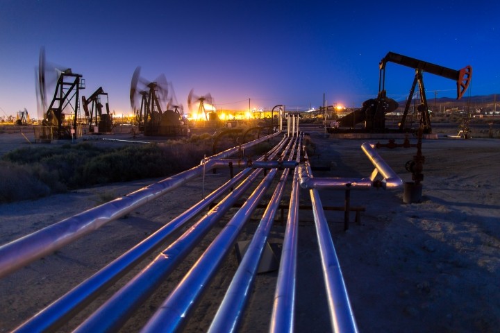 multiple pumpjacks illuminated against evening sky