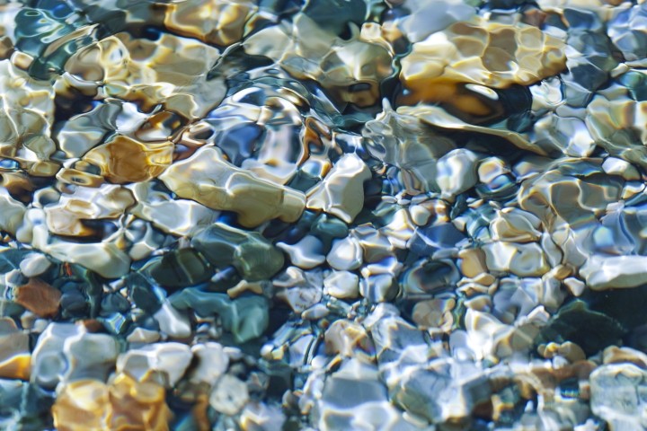 sunlight shining through water to illuminate multi-colored pebbles below