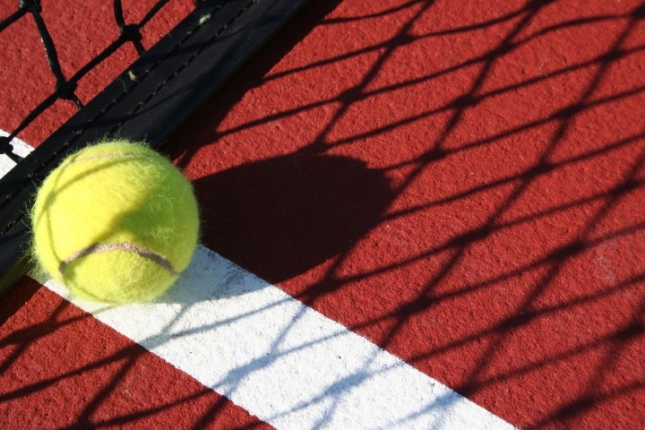 close up of yellow tennis ball on red court in shadow of net