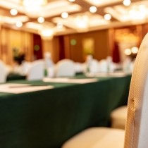 blurred view of large empty conference room with gold chairs and green tablecloths
